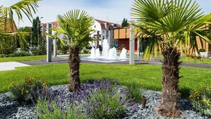 Un'area verde curata con palme, una fontana e un edificio dal design moderno.