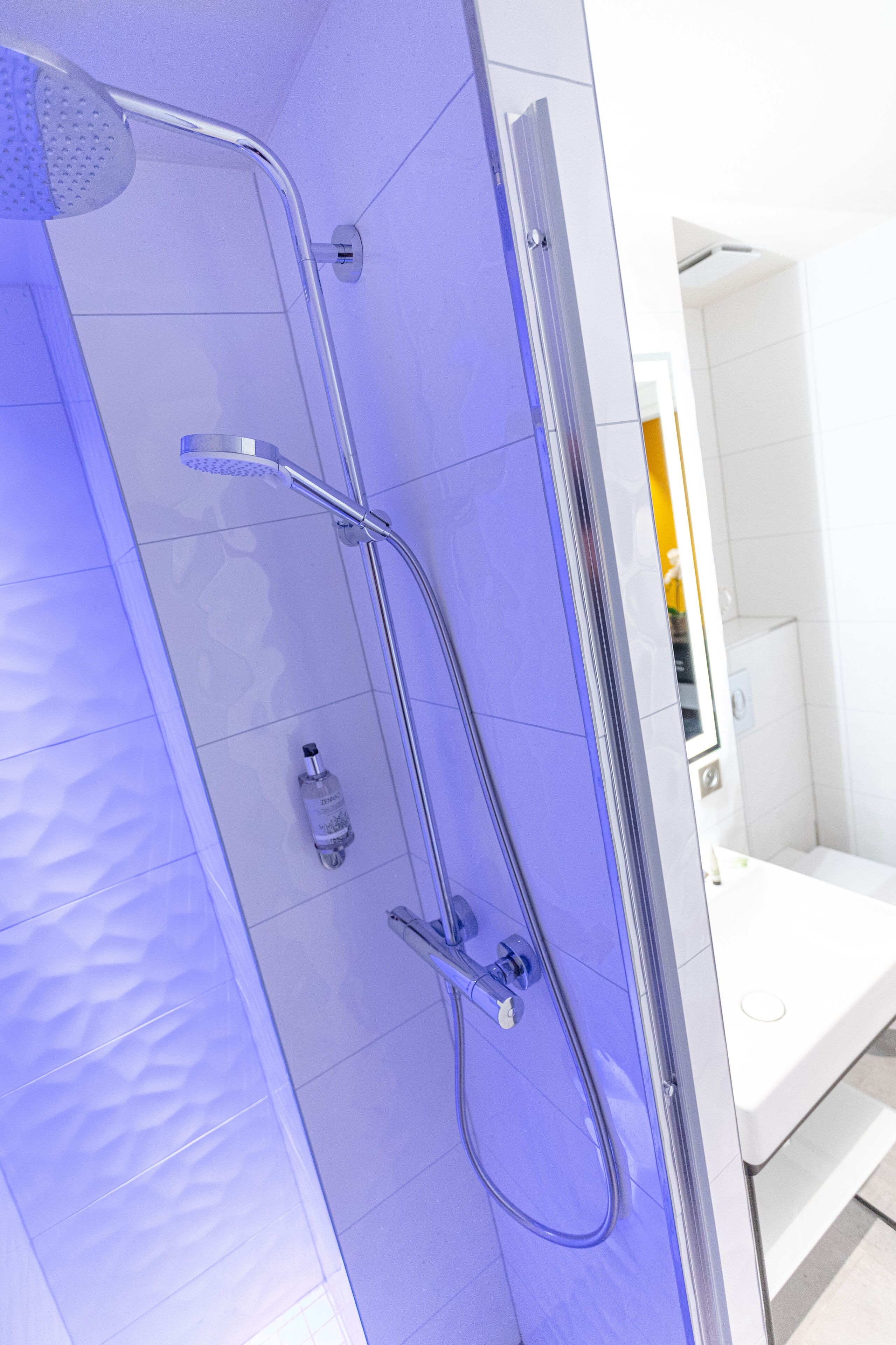 A modern bathroom with a glass-enclosed shower, white tiles, and a visible bottle of shampoo.