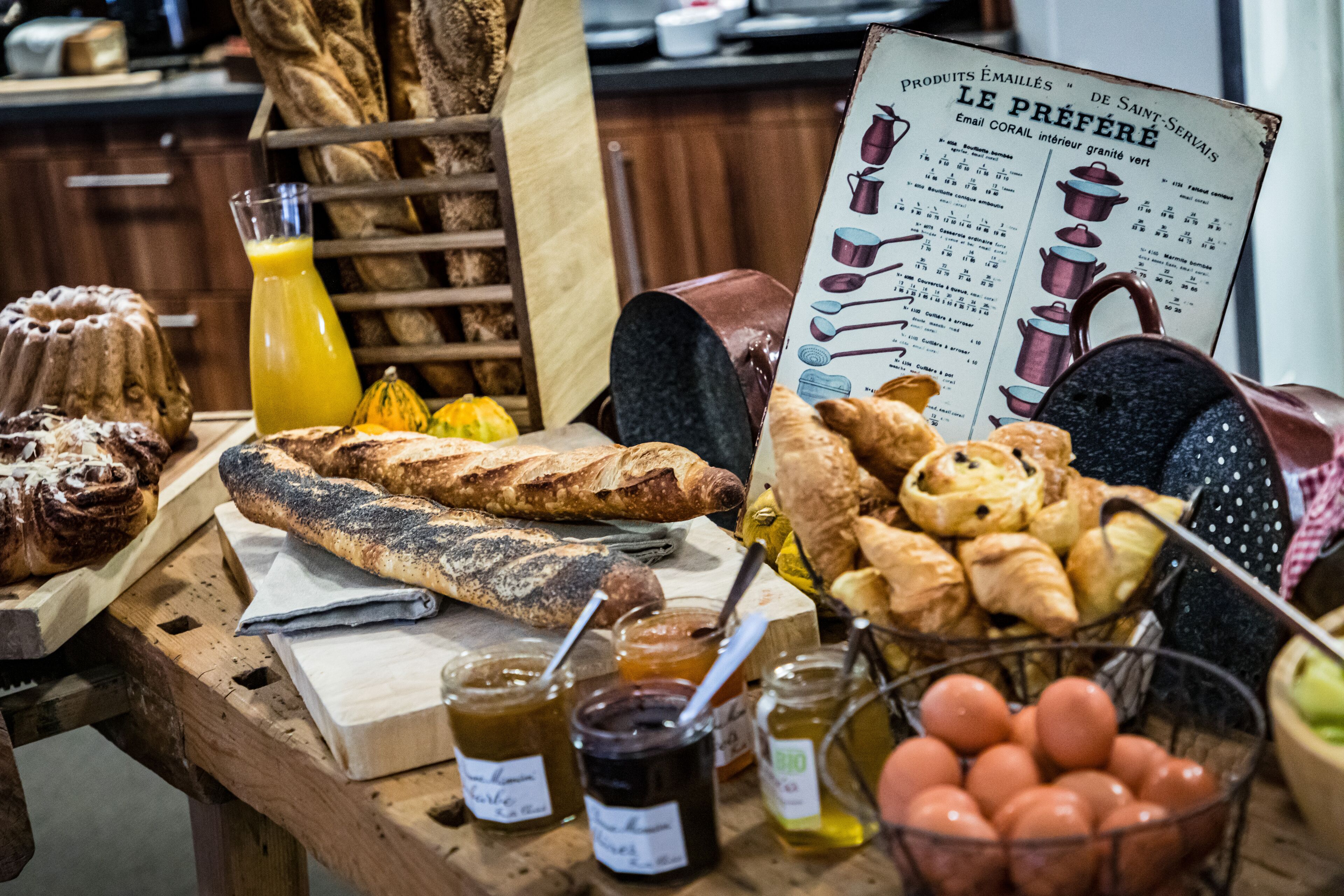 Een houten tafel met diverse gebakken producten, waaronder brood en gebak, en potten jam.