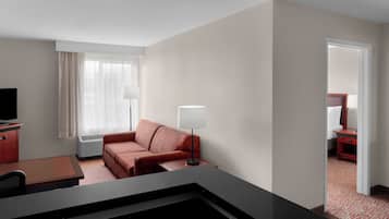 Una habitación de hotel con escritorio, un sofá rojo, una lámpara y televisión.
