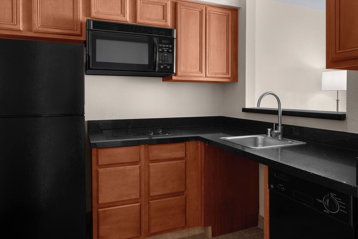 A kitchen with wooden cabinets, a black microwave, a sink, and a dishwasher.