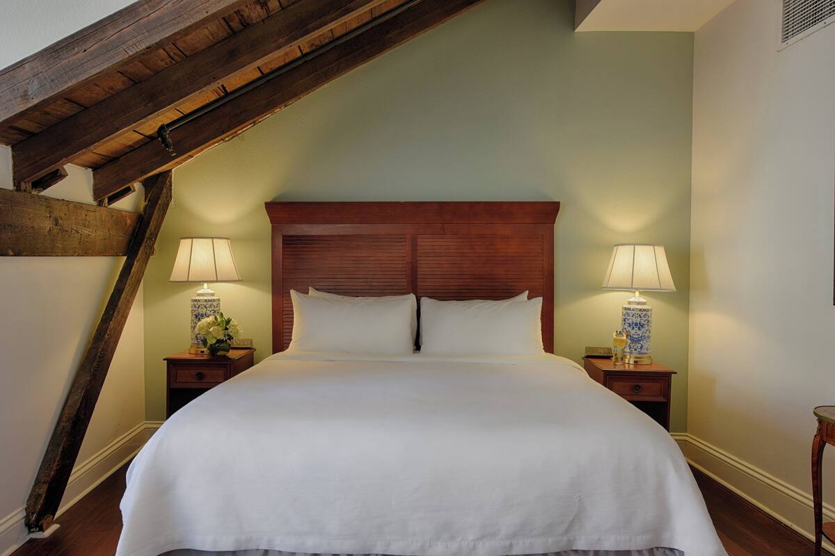 Una cama grande con cabecera de madera, dos mesitas de noche con lámparas y un techo inclinado.