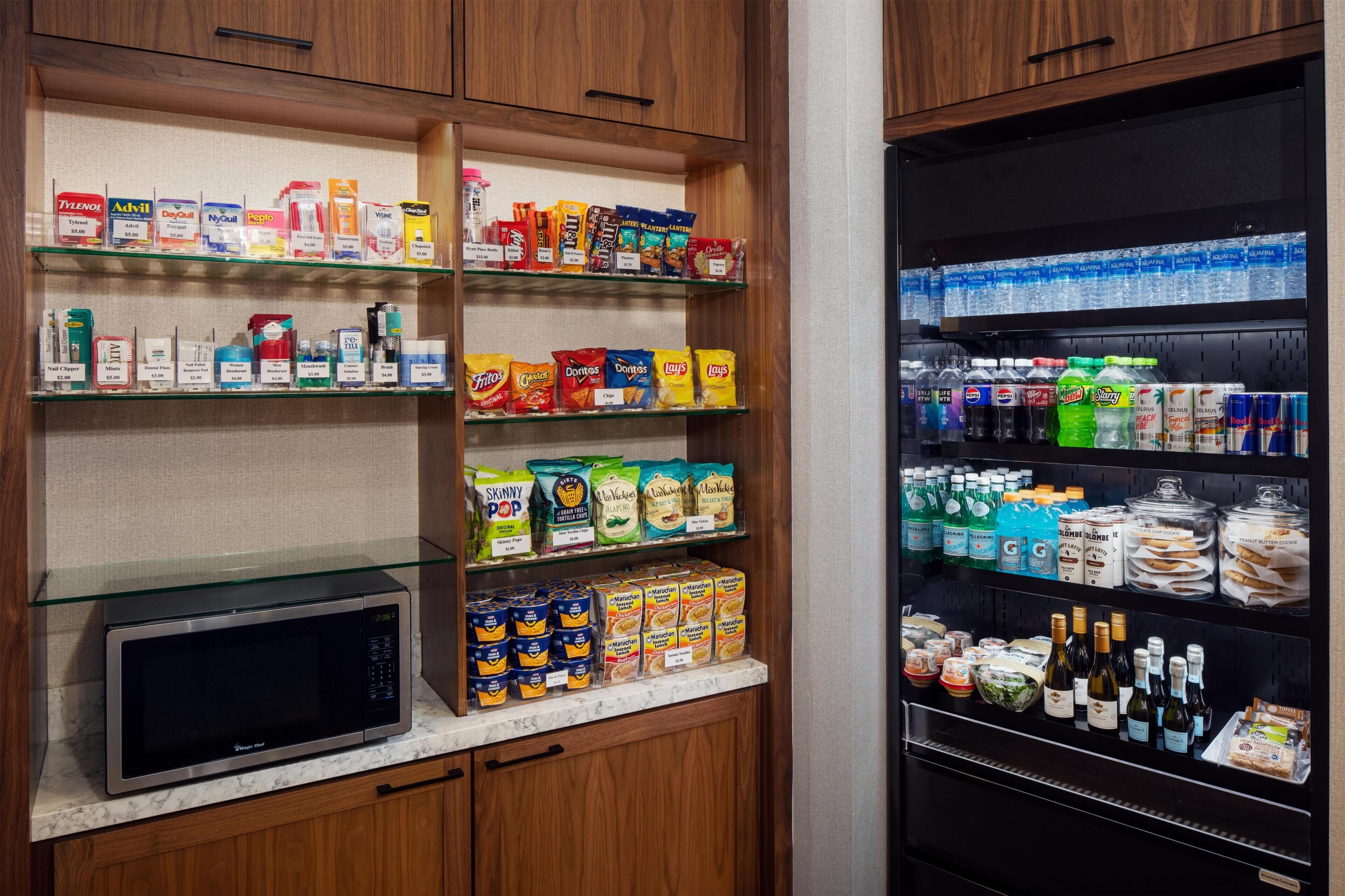 Una cocina con microondas, estantes llenos de refrigerios, bebidas y alimentos envasados.