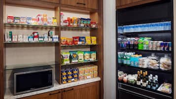 Una cocina con microondas, estantes llenos de refrigerios, bebidas y alimentos envasados.
