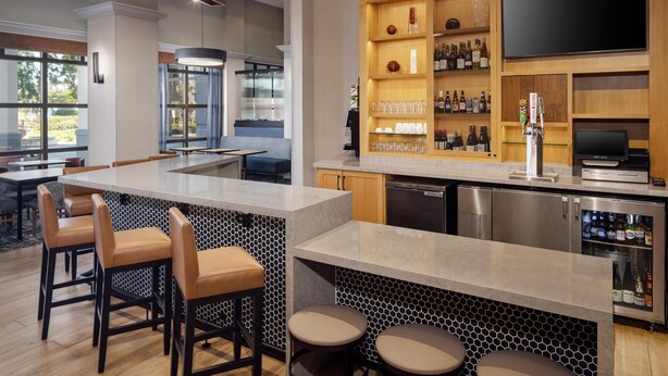 A modern kitchen with a bar area, bar stools, a refrigerator, and a television. - Hyatt Place Dublin/Pleasanton (Dublin)