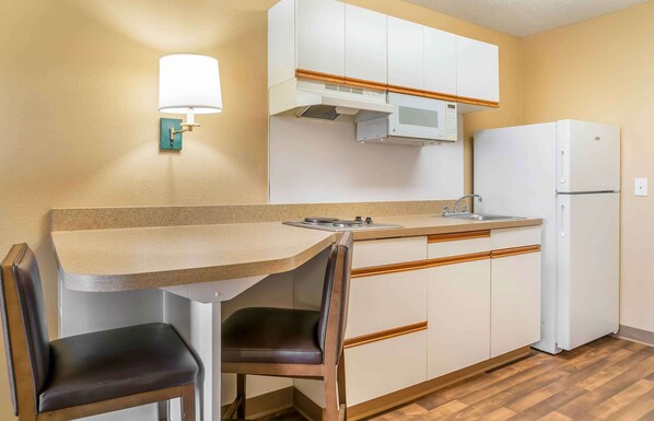A compact kitchen with a built-in stove, a microwave, and a refrigerator. - Auburn Hills Extended Stay Inn (Auburn Hills)