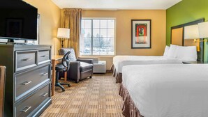 A hotel room with a bed, a desk with a chair, a television, a dresser, a window with curtains, and a framed picture on the wall. - Auburn Hills Extended Stay Inn (Auburn Hills)