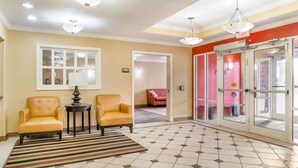 A lobby with two leather armchairs, a small table, a striped rug, a window with a white frame, and a red door with glass panels. - Auburn Hills Extended Stay Inn (Auburn Hills)