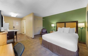 Relax in a cozy space with a neatly made bed, desk, and comfortable chair.
