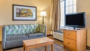A hotel room with a sofa, a wooden table, a TV on a wooden cabinet, a framed picture on the wall, and a window with curtains. - Auburn Hills Extended Stay Inn (Auburn Hills)