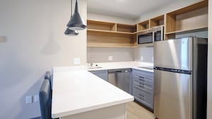 A modern kitchen with a stainless steel refrigerator, a built-in microwave, and wooden shelves above the countertop. - Candlewood Suites Beachwood Cleveland by IHG (Beachwood)
