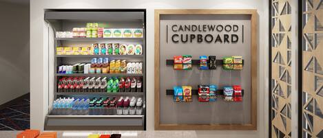 Un présentoir de boissons avec divers breuvages et en-cas, une enseigne indiquant « CANDLEWOOD CUPBOARD », et un panneau décoratif mural.