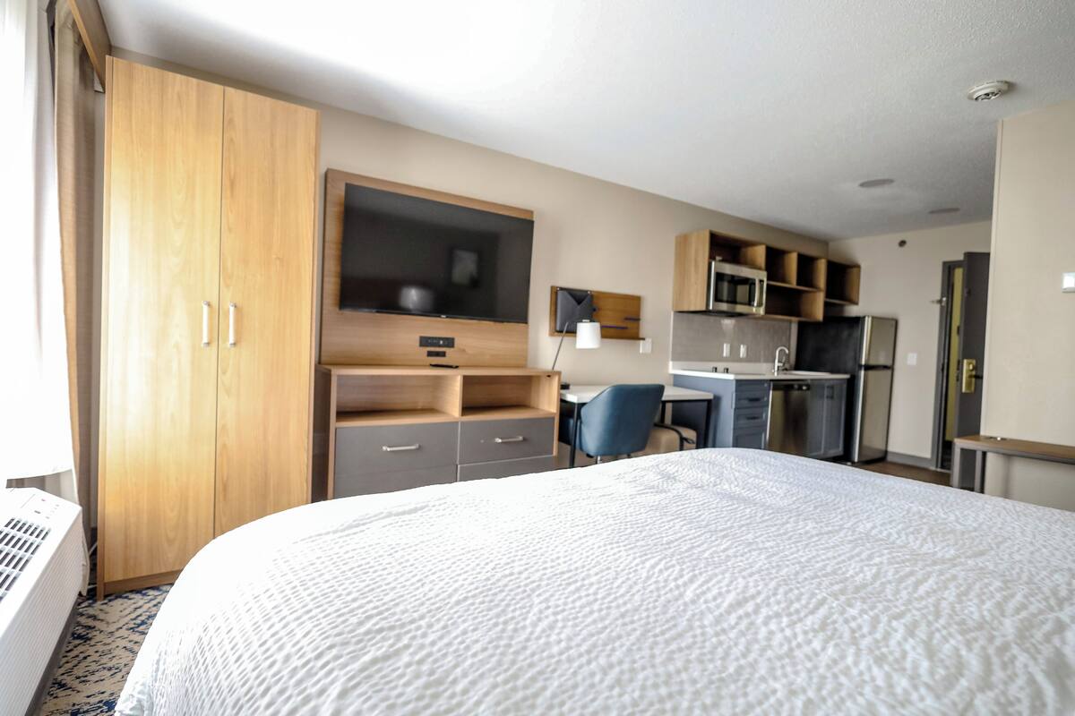 A hotel room with a large bed, a desk with a chair, a microwave, and a wardrobe.