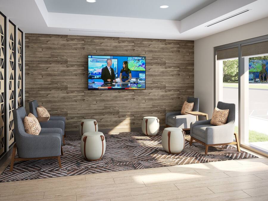 Um hall moderno com uma televisão grande exibindo uma transmissão de notícias, assentos confortáveis e vista para o exterior.