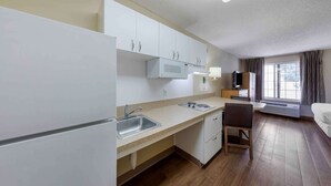 Ein kompaktes Hotelzimmer mit Küchenzeile, einem Bett, einem Schreibtisch und einem Fenster mit Vorhängen.