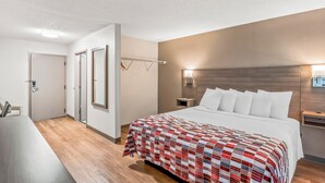 A hotel room with a large bed, a desk, and a mirror. - Red Roof Inn Southfield (Southfield)