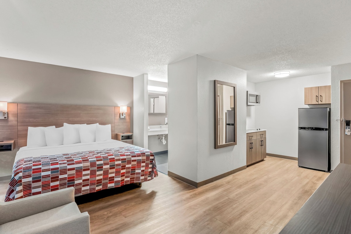 A modern hotel room with a large bed, a kitchenette, and a bathroom.