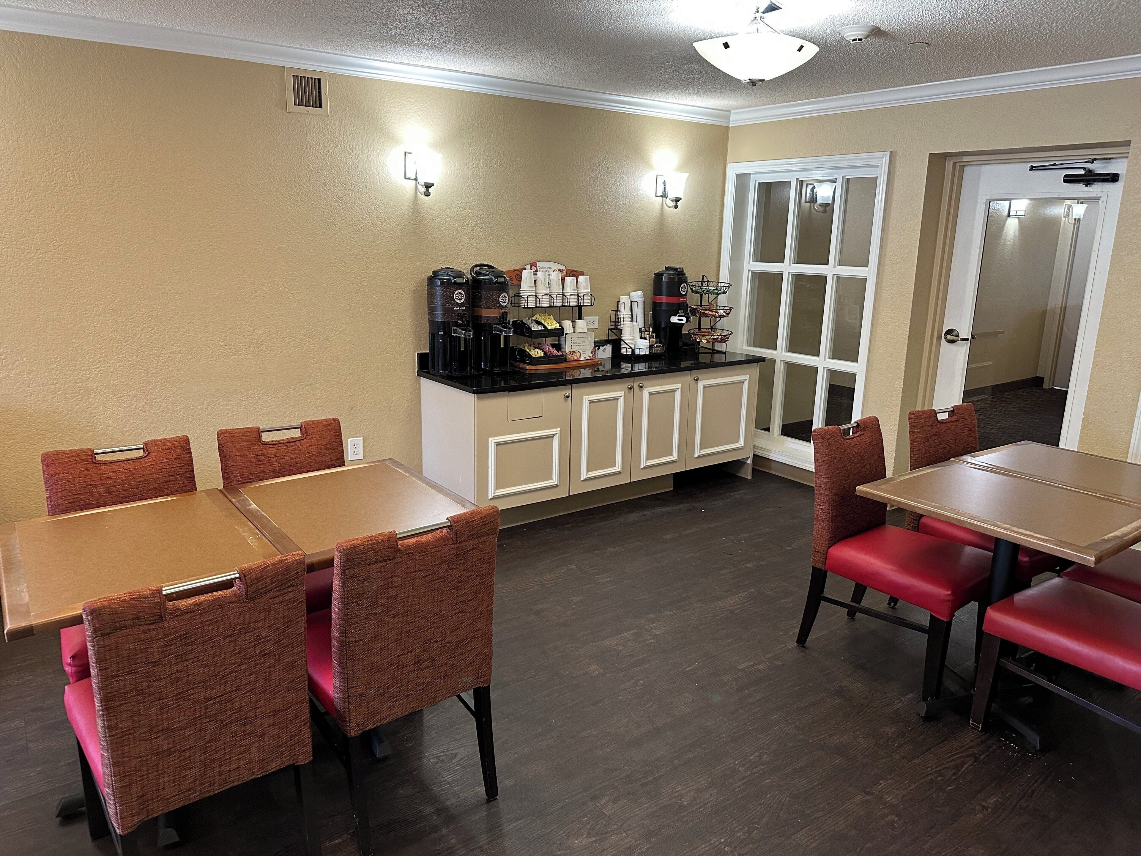 A dining area with tables and chairs, a coffee station with various coffee makers, and a door leading to another room.