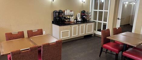A dining area with tables and chairs, a coffee station with various coffee makers, and a door leading to another room.