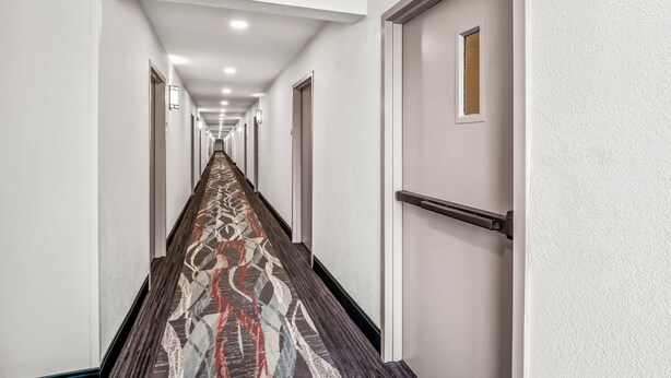 A long, narrow hallway with a patterned carpet and white walls. - Red Roof Inn Southfield (Southfield)