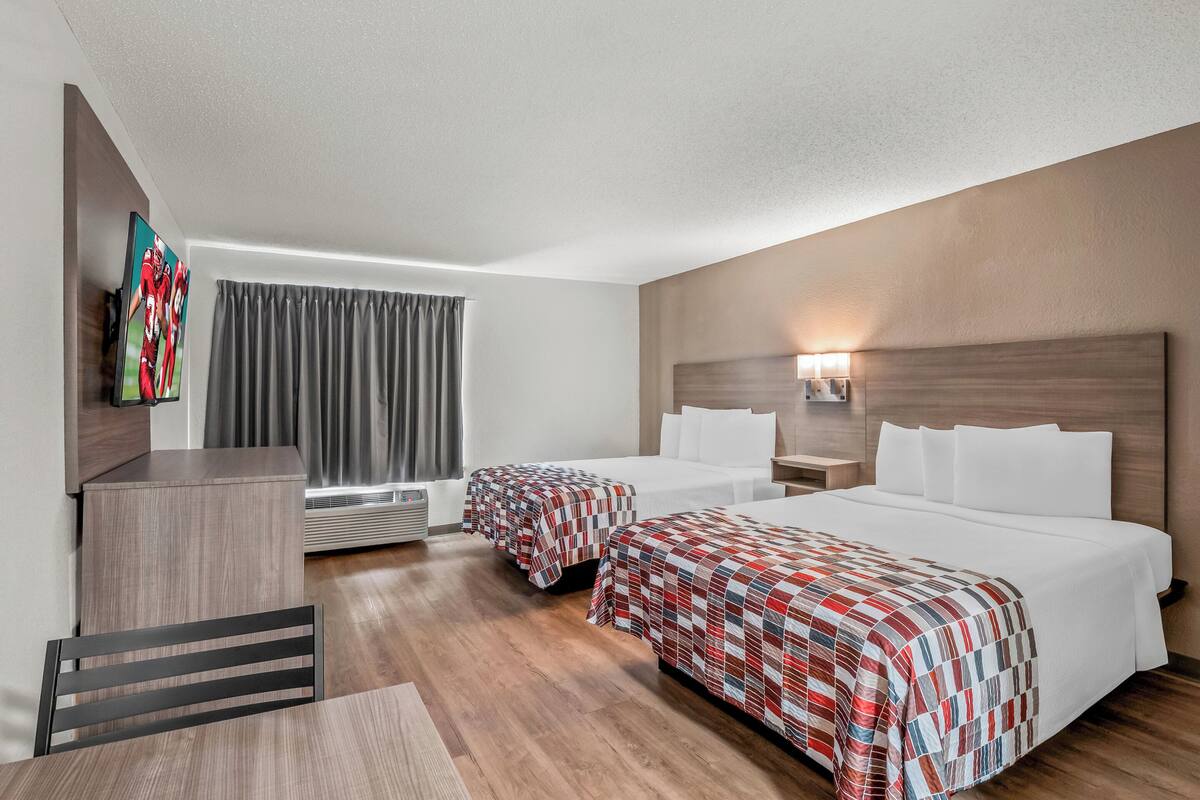 Ett hotellrum med två sängar, ett skrivbord, en stol, en TV och ett fönster med gardiner.