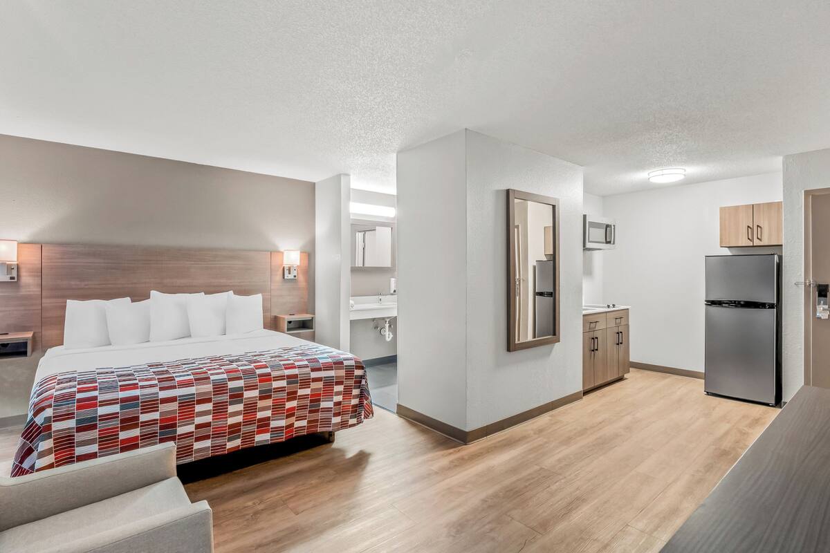 Ett modernt hotellrum med en stor säng, ett litet kök och ett badrum.