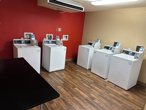 Una sala de lavandería con cuatro lavadoras, una mesa negra y una pared roja.