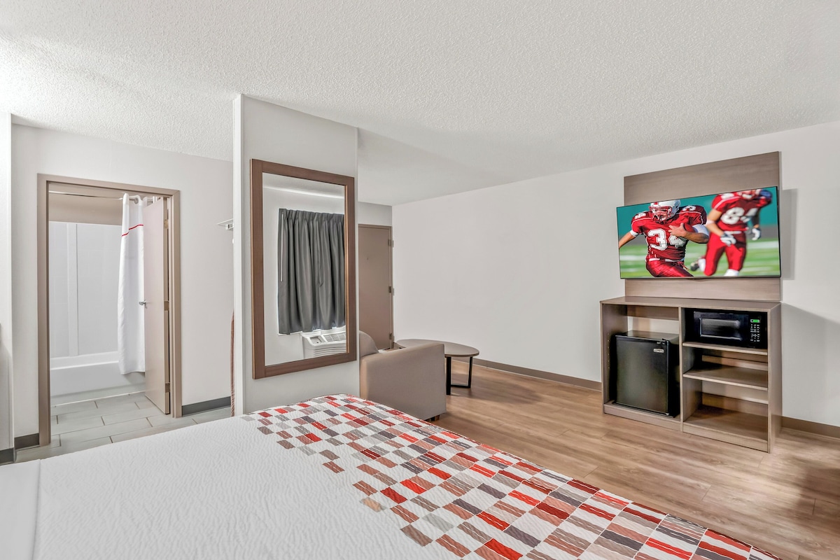 A hotel room with a large bed, a TV mounted on the wall, a microwave, and a small seating area.