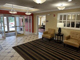 Un vestíbulo con alfombra a rayas, dos sillones, una lámpara y vistas al exterior a través de puertas de vidrio.