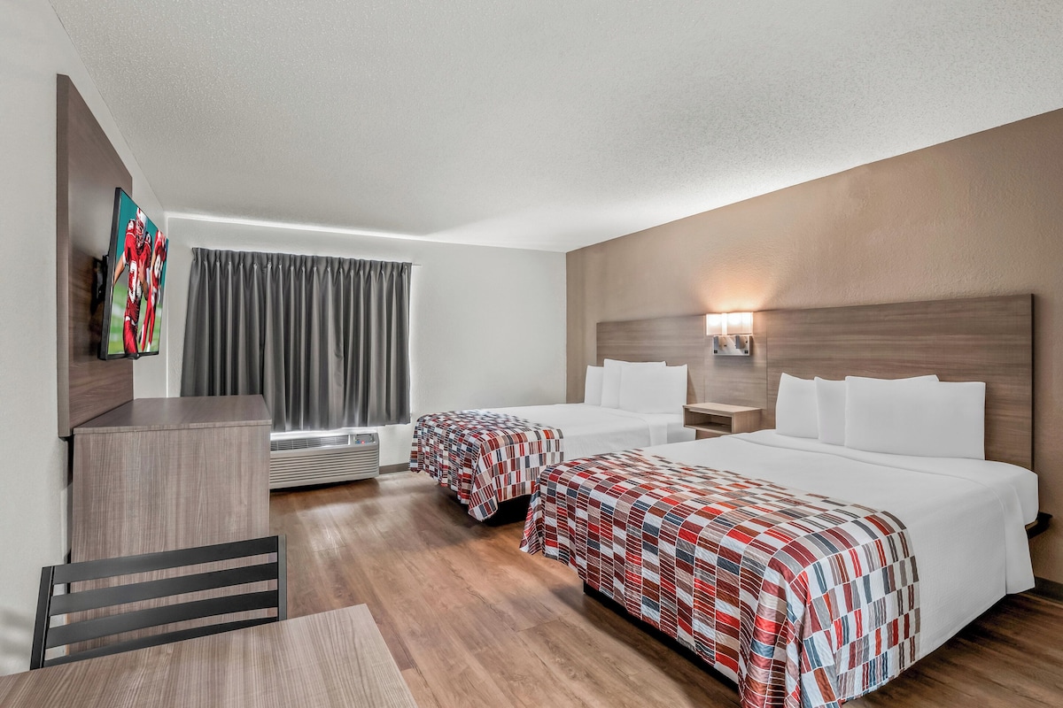 A hotel room with two beds, a desk, a chair, a TV, and a window with curtains.