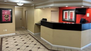 Un espace d’accueil d’hôtel comprenant un comptoir de réception, un panneau d’accueil encadré et une porte donnant sur un couloir.