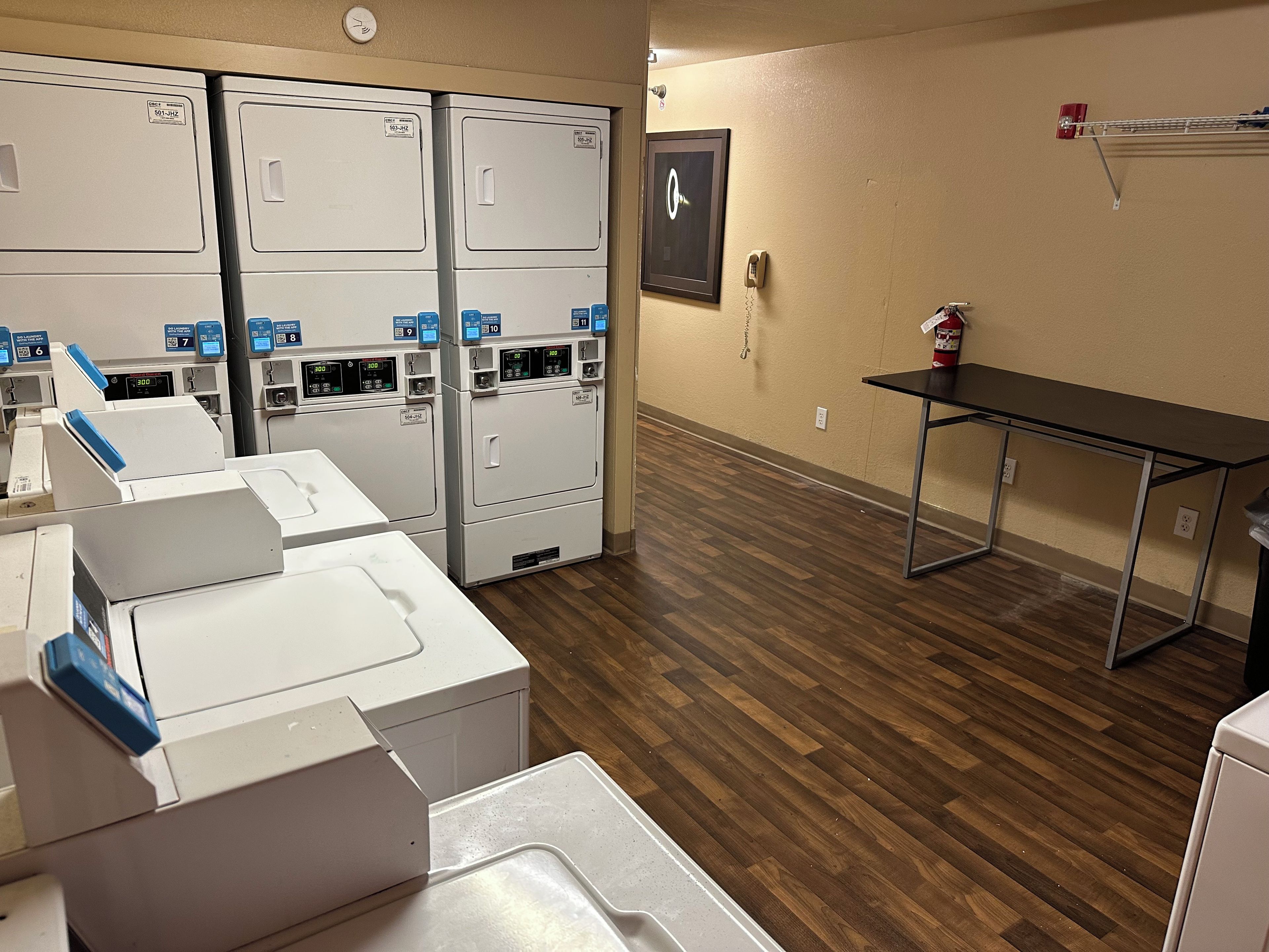 A laundry room with multiple washing machines, a fire extinguisher, and a clock on the wall.