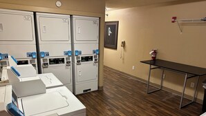 A laundry room with multiple washing machines, a fire extinguisher, and a clock on the wall. - Red Roof Inn Southfield (Southfield)