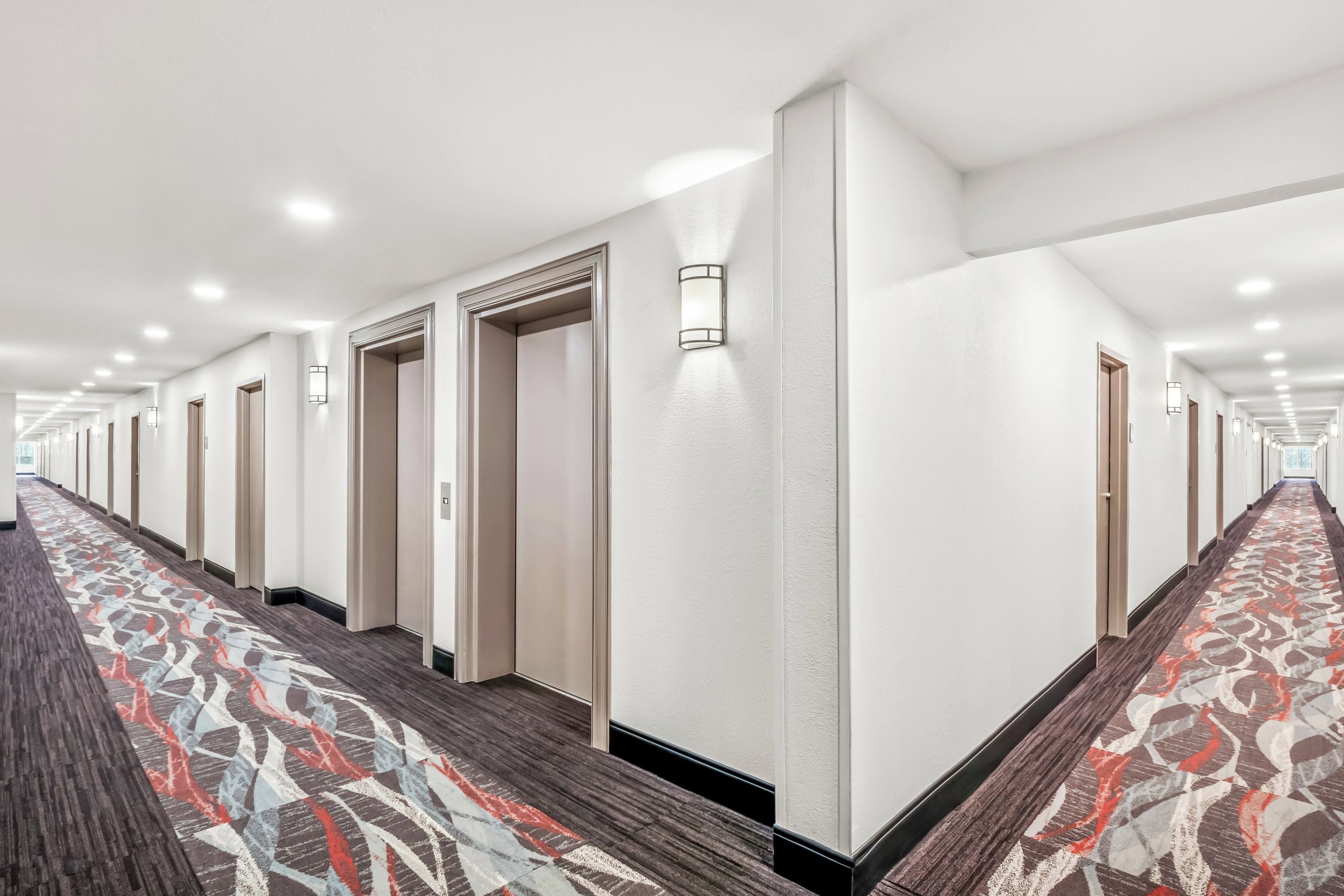 A long, well-lit hallway with patterned carpet and doors leading to rooms.