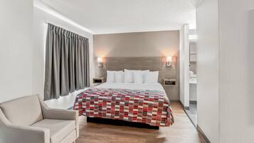 A hotel room with a bed, a chair, a nightstand, and a wall-mounted lamp.