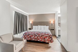 A hotel room with a bed, a chair, a nightstand, and a wall-mounted lamp.
