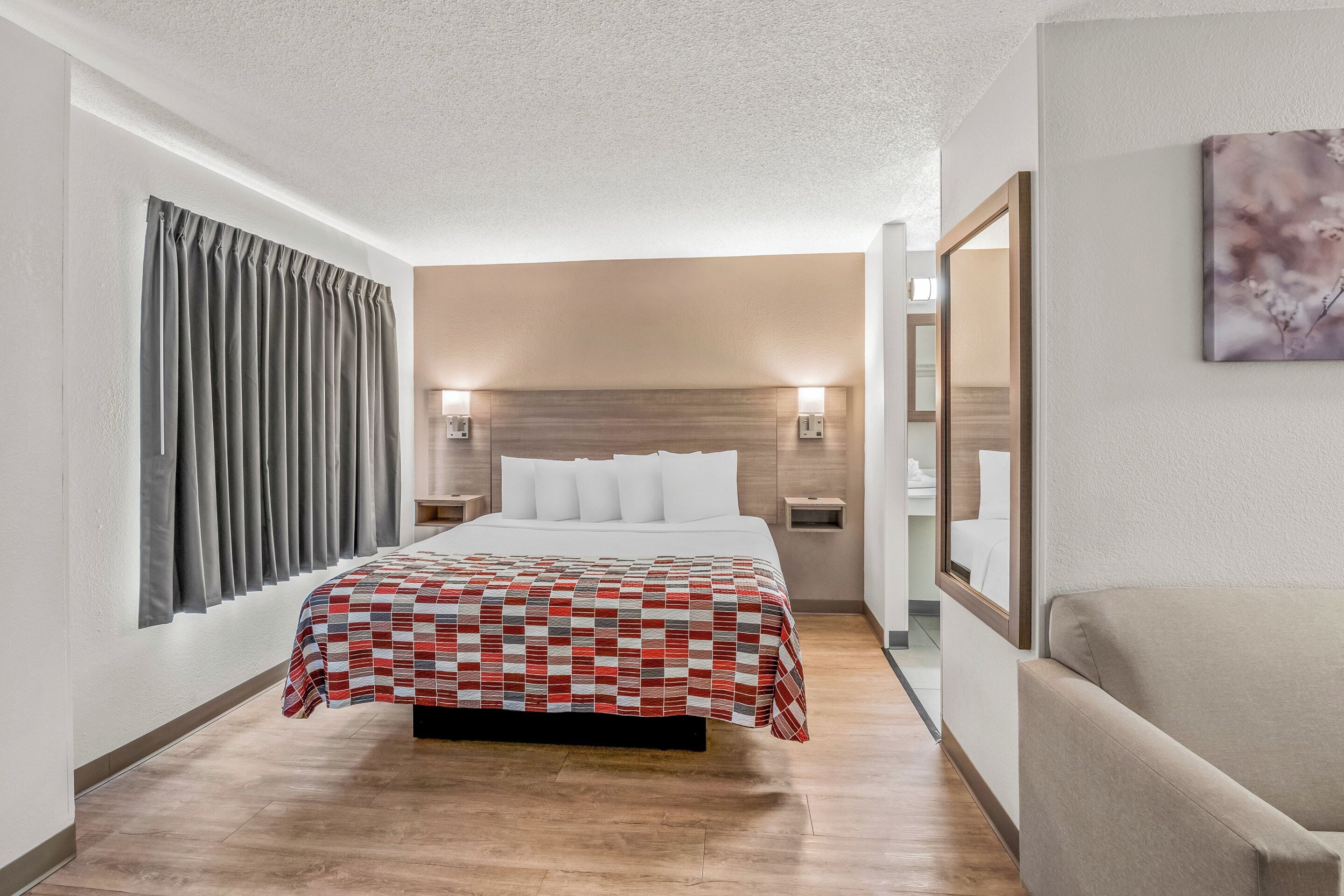 Ein Hotelzimmer mit Bett, Nachttisch, Spiegel und einem Wandbild.