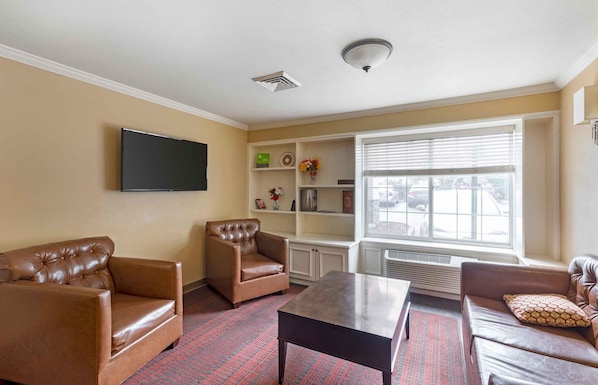 A living room with a flat-screen TV, leather sofas, a coffee table, and a window with blinds.