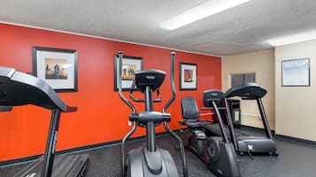 A gym with treadmills and elliptical machines, red walls, and framed pictures on the wall.
