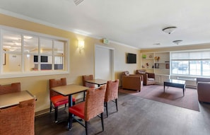 Habitación de hotel con comedor, sofá, televisor y ventana con persianas.