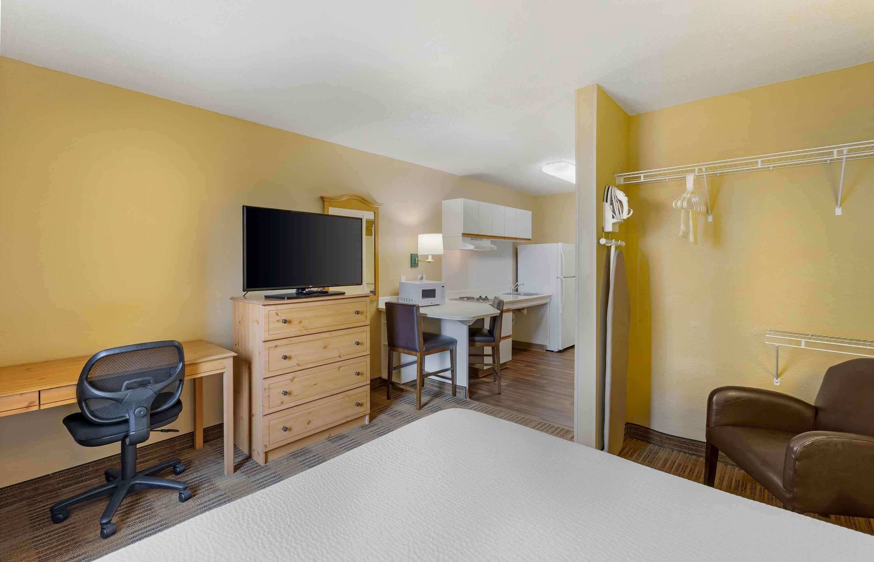 A hotel room with a bed, desk, chair, television, wardrobe, and a kitchenette.