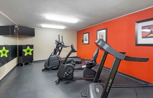 Une salle de sport équipée de tapis de course, de vélos d’appartement et d’un mur recouvert de miroirs.