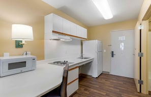 A compact kitchen with white cabinets, a microwave, a refrigerator, and a sink.