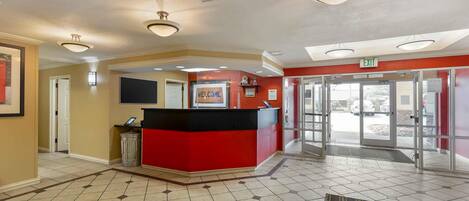A reception area with a red counter, a welcome sign, and an exit door.