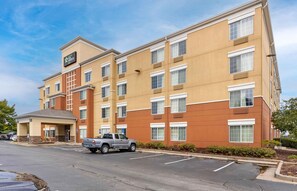 A multi-story hotel with a beige and brown facade, a covered entrance, and a parking lot with a truck.