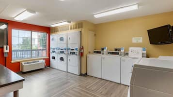 A laundry facility with multiple washing machines and dryers, a fire extinguisher, and a television mounted on the wall.