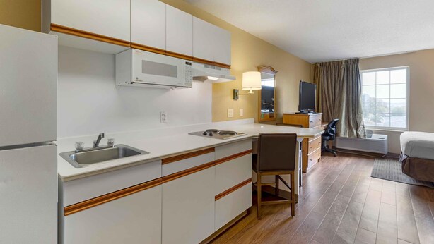 A compact hotel room with a kitchenette, a single bed, a desk, and a chair. - Extended Stay America Suites St Louis Westport Central (Maryland Heights)