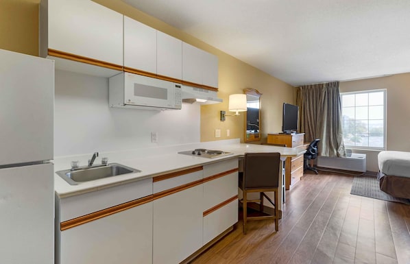Habitación de hotel compacta con kitchenette, una cama individual, escritorio y silla.