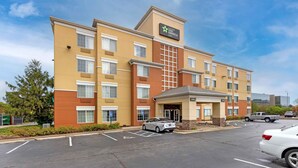 A multi-story hotel with a prominent Stay America sign, a lobby entrance, and a parking lot with several cars. - Extended Stay America Suites St Louis Westport Central (Maryland Heights)