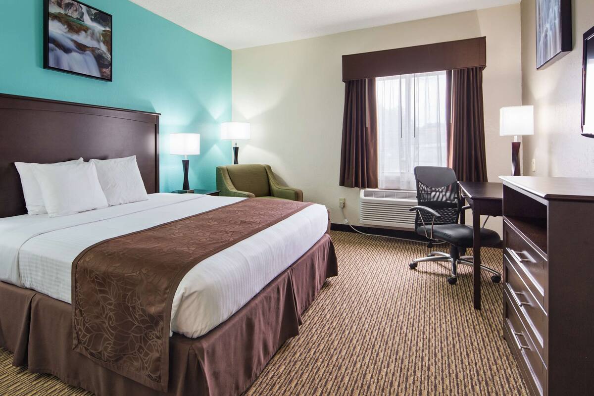 Une chambre d’hôtel avec un grand lit, deux tables de chevet, un bureau, une chaise et une fenêtre avec des rideaux.